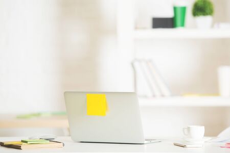 Back view of open laptop with sticker placed on modern office desktop with coffee cup, supplies and other itemsの写真素材