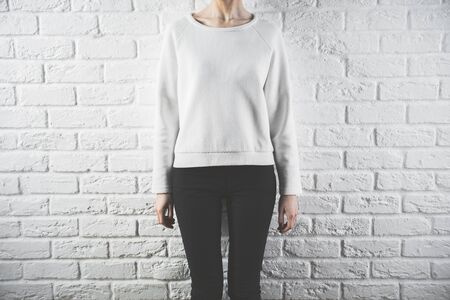 Front view of young woman in casual sweater. Retail concept. White brick wall backgroundの写真素材