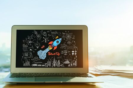 Close up of laptop wti space ship sketch on screen. Blurry city view background. Startup concept