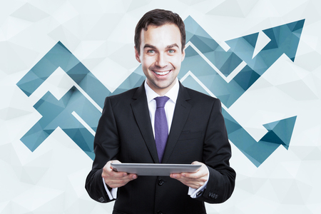 Cheerful businessman using tablet on polygonal background with upward chart arrows. Success conceptの写真素材