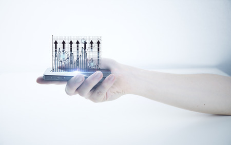 Side view of male hand holding cellphone with abstract business chart on light backgroundの写真素材