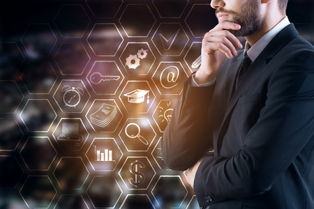 Side view of thoughtful young businessman in suit standing on blurry night city background with business icons in cells. Tech concept. Double exposureの写真素材
