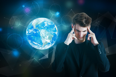 Pensive young businessman with digital globe on dark polygonal background. Technology concept.