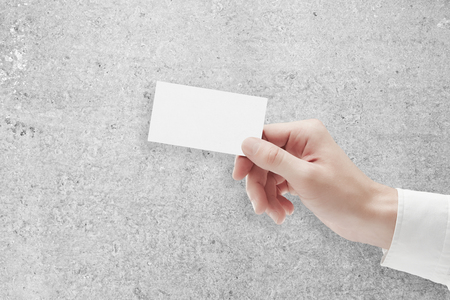 Close up of hand holding blank business card on concrete background. Mock up, Information conceptの写真素材