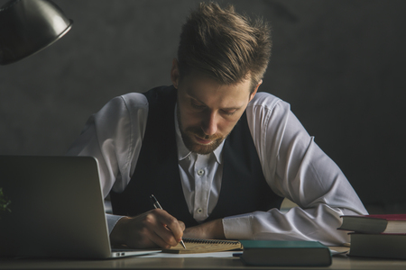 Handsome european male worker doing paperwork on desktop with electronic device and suppliesの写真素材