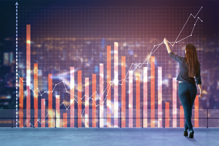 Back view of young woman drawing business chart hologram on concrete rooftop with night city background. Financial stock market concept. Double exposureの写真素材
