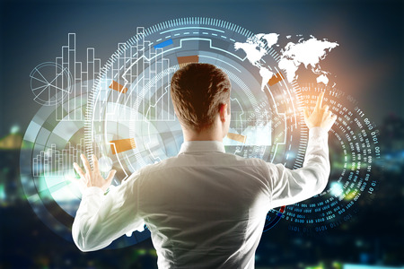 Back view of young businessman managing digital business buttons on night city background. Technology and infograph concept. Double exposureの写真素材