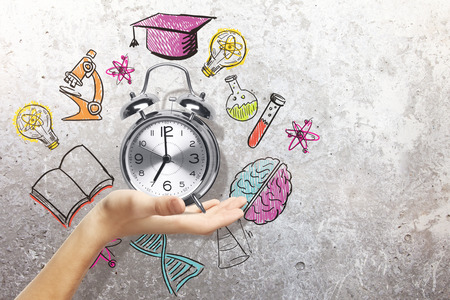 Hand holding silver alarm clock with abstract education sketch. Graduation conceptの写真素材