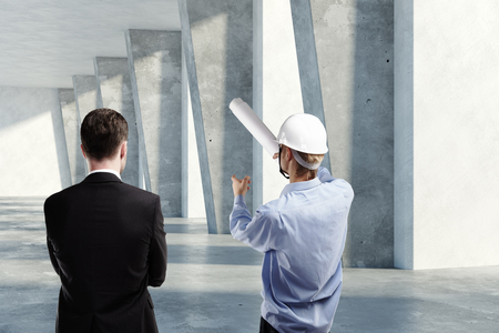 Businessman and engineer discussing project together in grunge concrete room interior with daylight. Teamwork concept. 3D Renderingの写真素材