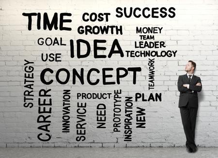Handsome businessman with folded arms standing in brick interior with business words on wall. Leadership conceptの写真素材