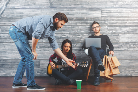 Happy friends playing the guitar, having fun and communication at home in wooden interior. Lifestyle conceptの写真素材