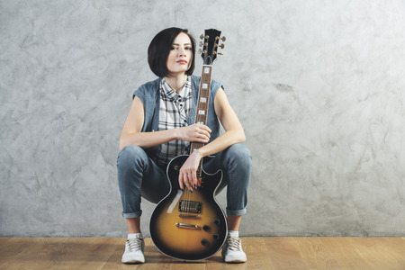 European woman with electric sunburst guitar and amplifier sitting in studio room with wooden floor and concrete wall. Musician, concert, hobby, leisure, rehearsal conceptの写真素材