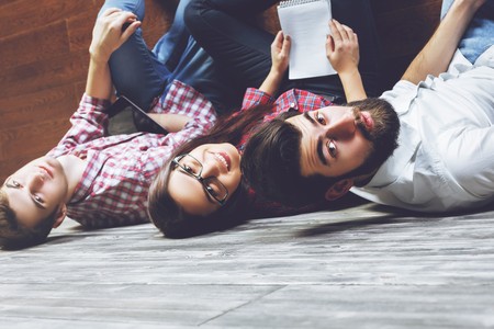Top view of two young european businessmen and woman sitting on floor of wooden room. Team, meeting conceptの写真素材