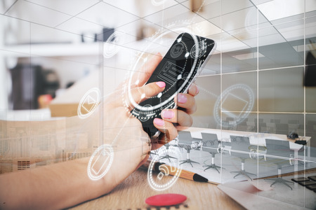 Side view of woman hand using smartphone with digital business hologram at modern office desk....
