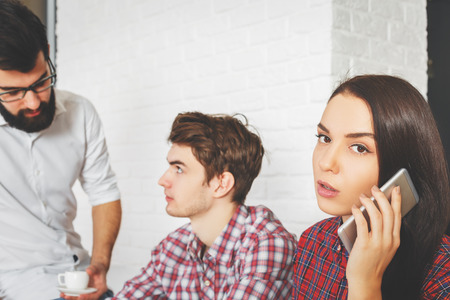 Side portrait of attractive european woman and men talking on the phone at workplace. White brick wall background. Communication conceptの写真素材