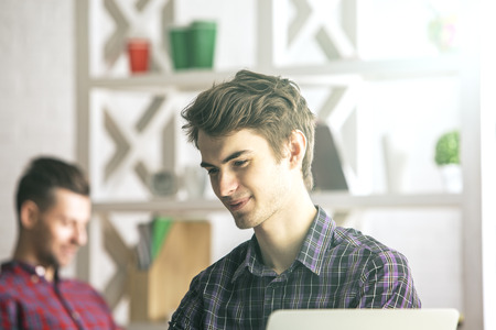 Blurry close up portrait of two handsome smiling european men at workplaceの写真素材