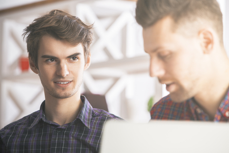 Blurry close up portrait of two handsome smiling european colleagues at workplaceの写真素材