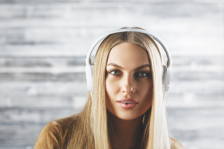 Portrait of beautiful european woman with headphones on wooden wall background. Music, fun, hobby, leisure conceptの写真素材