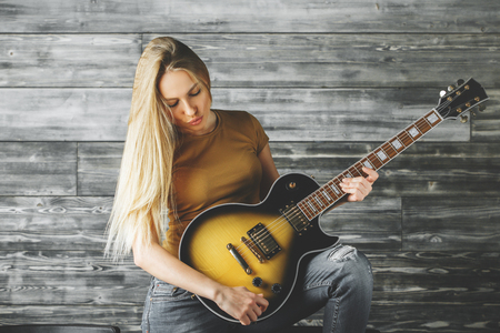 Portrait of attractive young woman playing the guitar in studio with wooden wall. Music, hobby,...