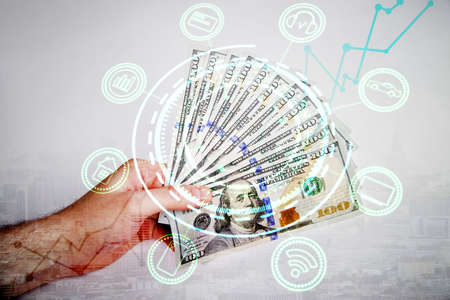 Male hand holding dollar banknote fan on city background with abstract smart hologram. Digital money...
