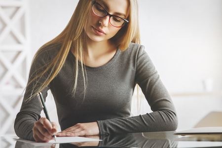 Portrait of attractive young woman doing paperwork at modern office desk with items. Secretary, accounting, project conceptの写真素材