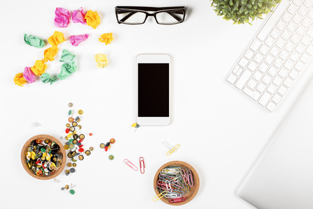 Top view of white office desk with blank smartphone, supplies, laptop keyboard and other items. Phone advertisement concept, Mock upの写真素材