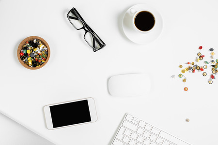 Top view and closeup of white office desktop with empty smartphone, coffee cup, supplies, laptop keyboard and other items. Mock upの写真素材