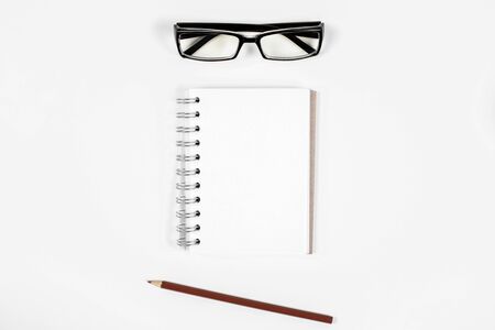 Top view of white office desktop with empty spiral notepad, glasses and pencil. Mock upの写真素材