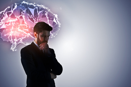 Thoughtful young european businessman on gray background with digital polygonal brain and copy space. Artificial intelligence conceptの写真素材
