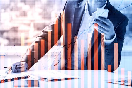 Businessman using smartphone at workplace with paperwork and business chart bars. Economy and...