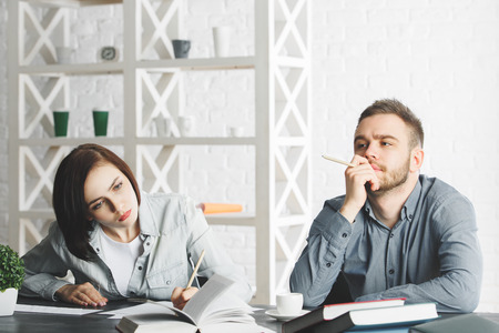 Attractive businessman and woman doing paperwork at office desk with pile of books. Partnership concept の写真素材
