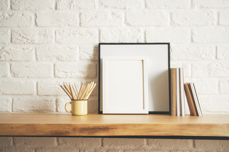 Front view of wooden desk with empty picture frame, notepads and iron mug with pencils. Decor, decoration and style concept. Mock up の写真素材