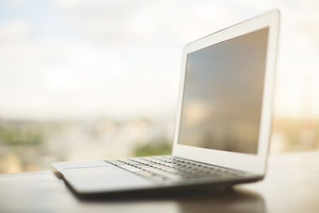 Close up and side view of empty laptop placed on desk with blurry city view. Mock upの写真素材