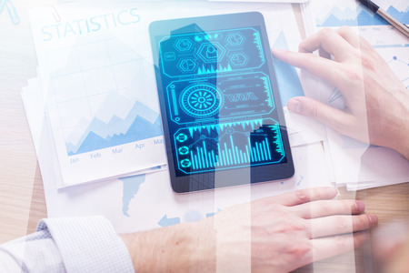 Top view of businessman hands using tablet with business interface placed on office desk with...