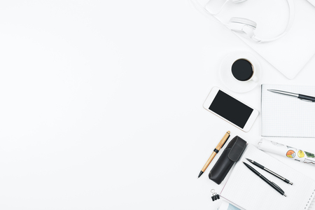 Top view and close up of modern white office workplace with empty smartphone, supplies, headphones and other items. Leisure, hobby, break, work and occupation concept. Mock upの写真素材