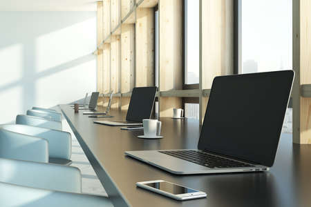 Side view of modern coworking interior with laptops, coffee cups and city view with daylight. Mock...