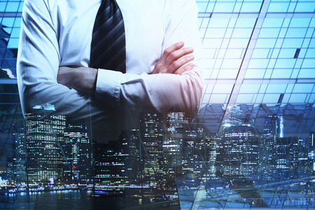Unrecognizable businessman with folded arms on abstract night city background. Tomorrow and employment concept. Double exposureの写真素材