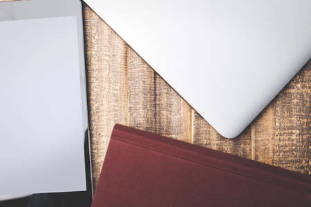 Top view of wooden desktop with glossy tablet, closed laptop, book and copy space. Creative backgroundの写真素材