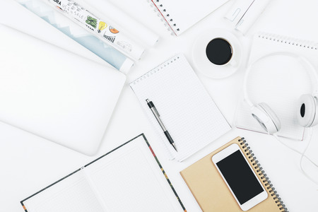 Top view and close up of modern white office workspace with empty smartphone, supplies, headphones...