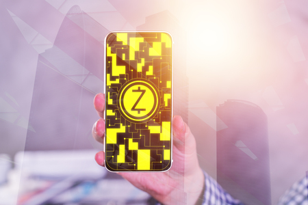 Hand holding smartphone with abstract Z coin on city background. Cryptocurrency concept. Double exposureの写真素材