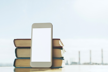 Close up of blank white smartphone leaning on stack of books on blurry city background. Mock up, Education concept の写真素材