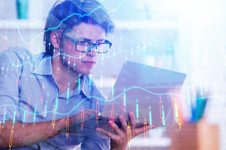 Attractive young european businessman using laptop with abstract forex chart. Investment and economy...