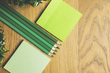 Top view of wooden desktop with empty green stickers, pencils and decorative plants. Mock up の写真素材