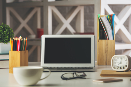 Close up of modern designer desktop with blank laptop screen, coffee cup, supplies and other items. Workplace concept. Mock up の写真素材