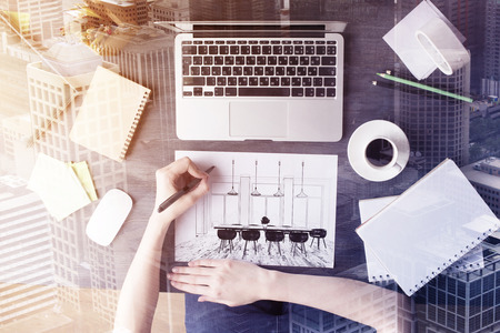 Top view of female hands drawing meeting room blueprint on desk with laptop, coffee cup and other...