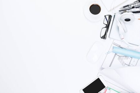 Top view of white office desktop with architectural sketch, supplies and other items. Blueprint and...
