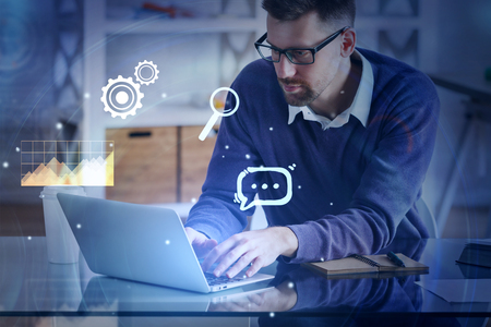 Handsome european businessman using laptop at abstract workplace with digital business interface. Media and finance concept. Double exposure の写真素材