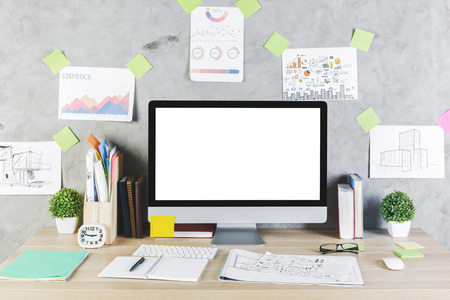 Close up of creative designer workplace with empty computer screen, supplies and other items on concrete wall background. Mock up の写真素材