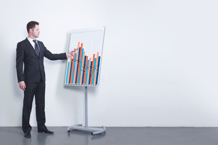 Businessman delivering presentation on business in simple concrete room interior with sketch on whiteboard stand. Workshop and strategy concept. 3D Rendering の写真素材