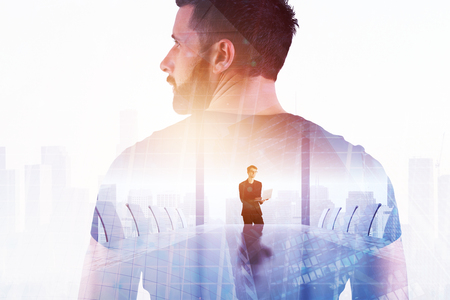Success and leadership concept. Thoughtful young businessman standing on abstract creative city office background with sunlight and copy space. Double exposure の写真素材